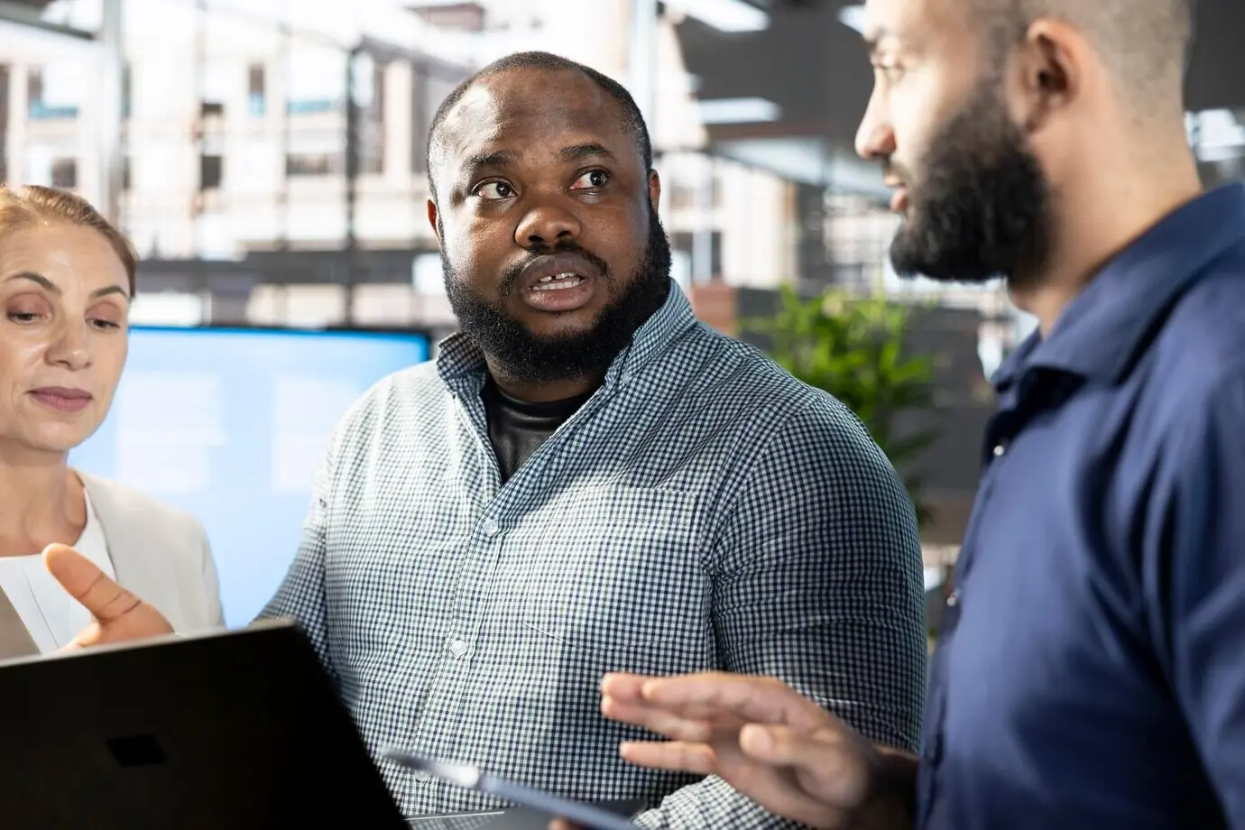 Gerente mirando la pantalla de un portátil mientras los trabajadores le muestran datos de investigación.